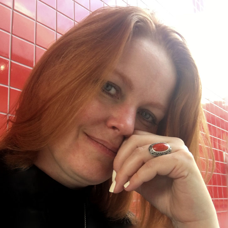 Portrait of illustrator Majken Sander sitting in front of a red tile wall